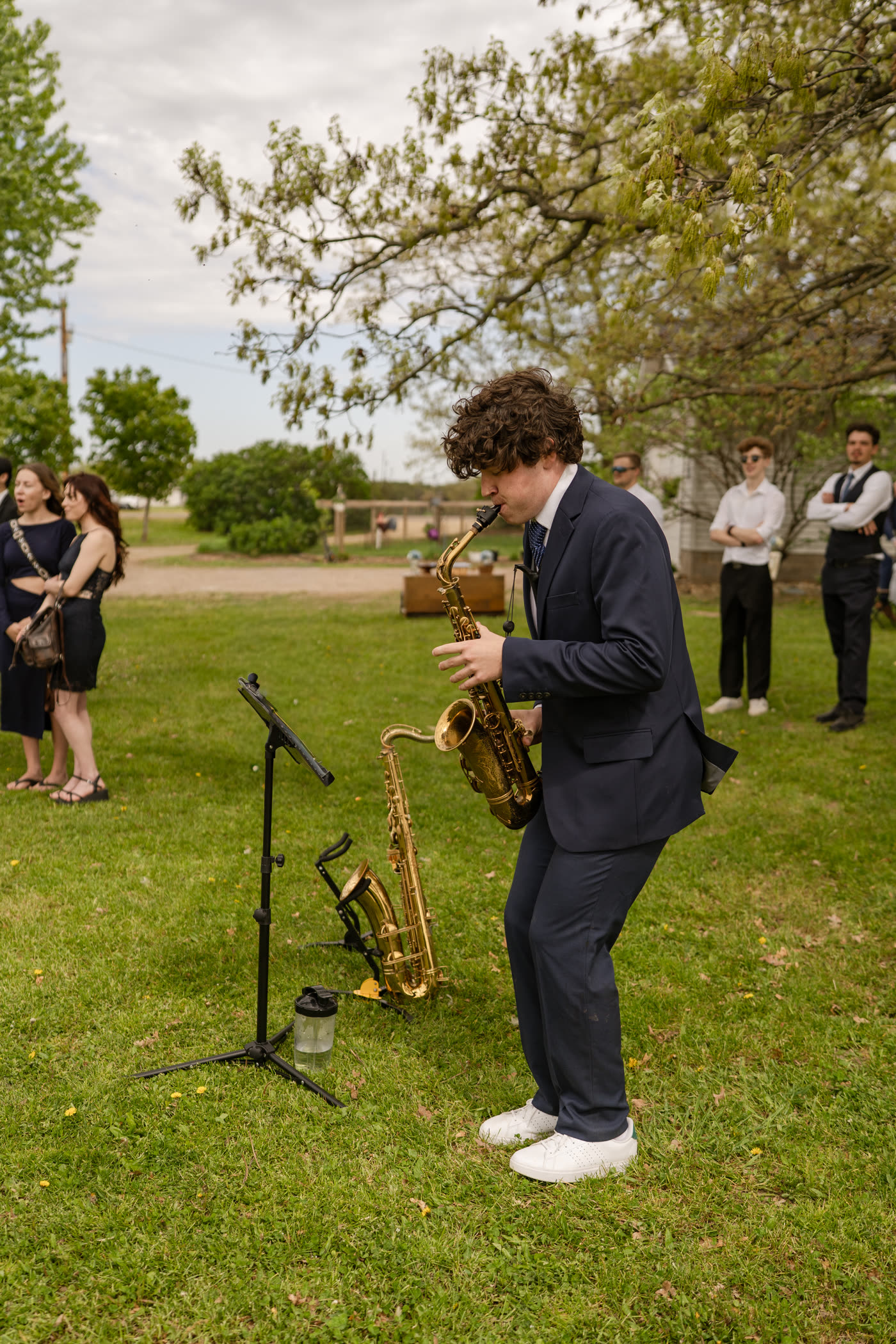 Liam Jakubowski playing saxophone at a wedding, guests behind him on the lawn